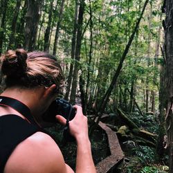 Rear view of woman photographing in forest