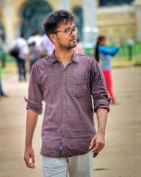 Young man looking away while walking on footpath in city