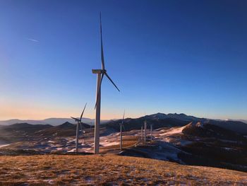 Wind turbines on landscape against clear blue sky