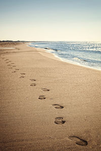 Footprints on sand at beach against sky