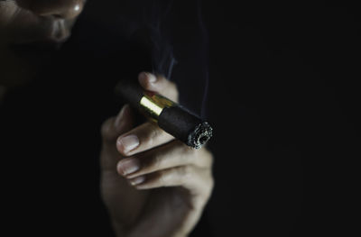 Close-up of woman holding cigarette against black background