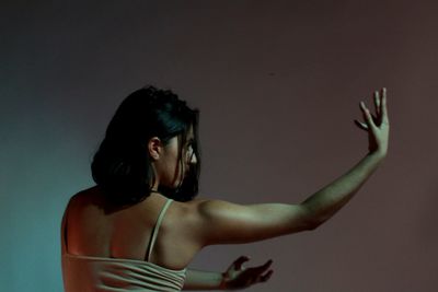 Rear view of young woman dancing against wall