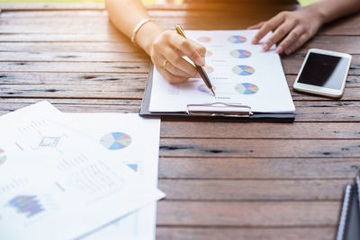 Cropped hands of woman analyzing graphs by mobile phone on table