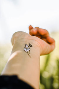 Cropped hand of woman with tattoo against clear sky