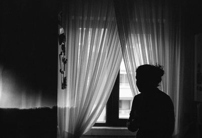 Silhouette woman looking through window at home