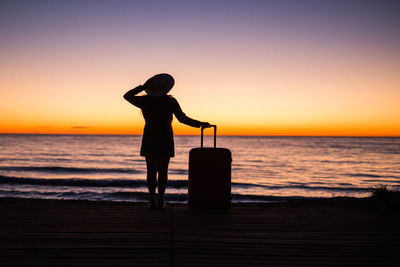 Silhouette woman standing on beach against sky during sunset