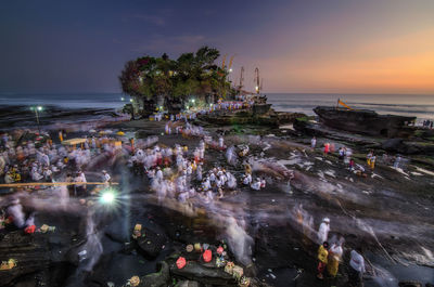 Blurred motion of people at beach against sky during sunset