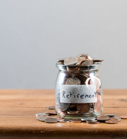 Close-up of coins in jar on table against white background