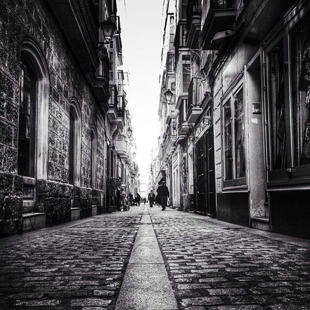 architecture, building exterior, built structure, the way forward, diminishing perspective, street, city, vanishing point, cobblestone, building, sky, residential building, incidental people, city life, walking, residential structure, transportation, day