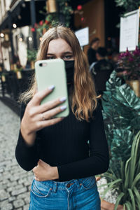 Young woman having video call talking while walking downtown wearing the face mask to avoid virus