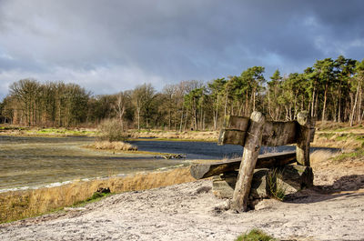 Wooden bench on a sandy beach by a lake under sunny, yet cold and windy weather circumstances