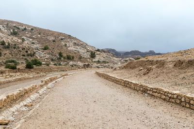 Dirt road leading towards mountains against sky