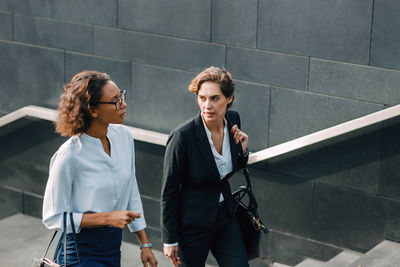 Young woman using mobile phone while standing against wall