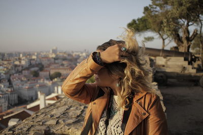 Woman with hand in hair standing by retaining wall against sky