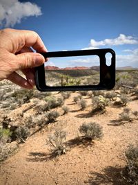 Close-up of hand holding phone cover in desert against sky