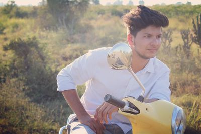 Young man sitting on motor scooter during sunny day