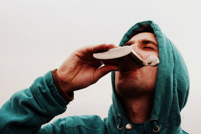 Close-up of man drinking from hip flask against clear sky