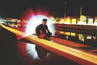 Young man sitting on illuminated bridge