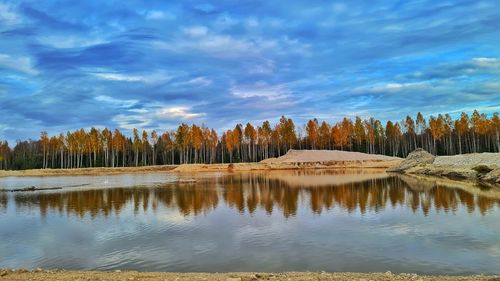 Reflection of trees in lake against cloudy sky