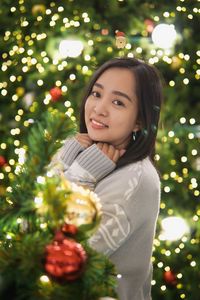 Portrait of young woman standing by christmas tree