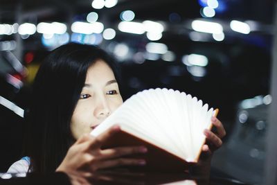 Young woman holding book against illuminated lights at night