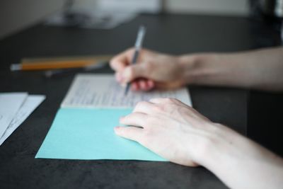 Cropped image of person holding paper with pen on table