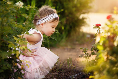 Side view of cute girl looking down while crouching against plants on field