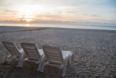 Chairs on beach against sky during sunset