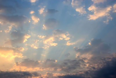 Low angle view of sunlight streaming through clouds