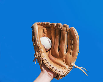 Close-up of human hand wearing glove holding ball while playing baseball against clear blue sky