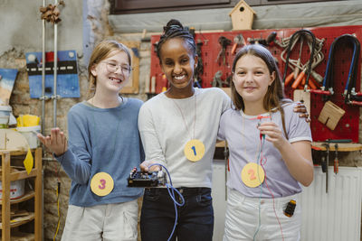 Portrait of happy female students showing electrical parts during technology workshop at school