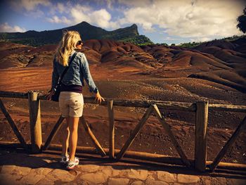 Rear view woman with hand in hair standing by railing against landscape