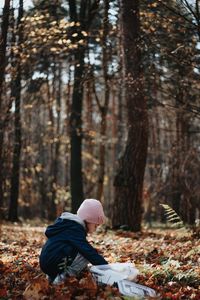 Side view of girl crouching in forest during autumn