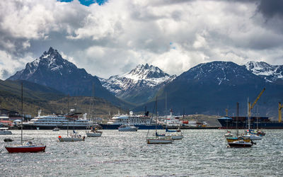 Sailboats moored on river by snowcapped mountains against sky