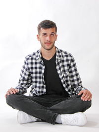 Full length of young man sitting on white background