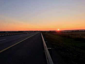 Road leading towards landscape against clear sky during sunset