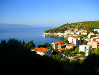 Scenic view of townscape by sea against clear blue sky