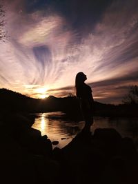 Silhouette man standing on lake against sky during sunset