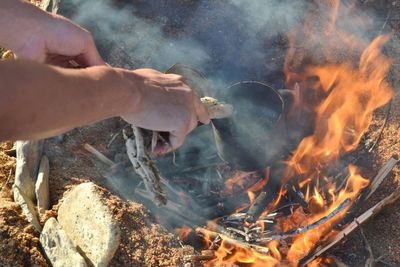 Cropped hands holding containers over campfire