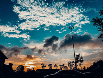 Silhouette trees by street against sky during sunset