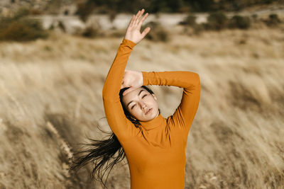 Beautiful woman with arms raised standing in field during windy day