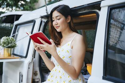 Close-up of smiling woman reading book standing by motor home