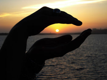 Silhouette hand holding sun over sea during sunset