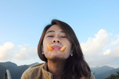 Portrait of woman with orange slices in mouth against sky