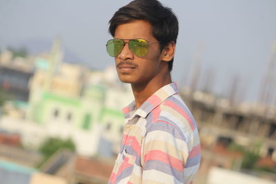 Portrait of young man standing against sky in city