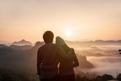 Rear view of man looking at mountains against sky during sunset