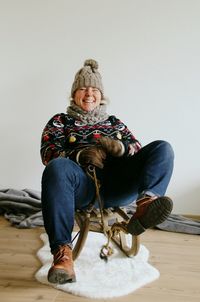 Young woman sitting on sled against wall