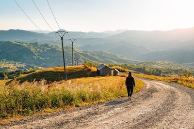 Rear view of man on country road against mountain range at sunset during autumn