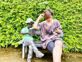 Woman using smart phone while sitting by statue