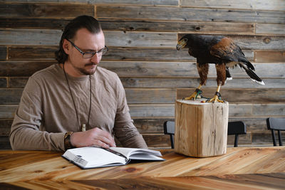 Man is working, writing with wild bird at home by the table. making noted, memories, diary with
